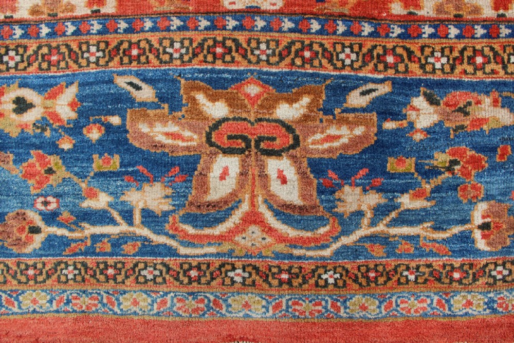 A large hand-knotted antique Ziegler carpet featuring a terracotta red field with floral palmettes framed by a wide indigo blue border. View II