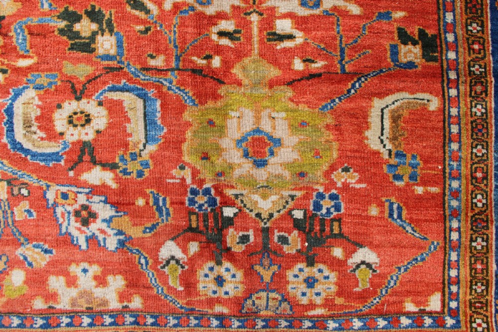 A large hand-knotted antique Ziegler carpet featuring a terracotta red field with floral palmettes framed by a wide indigo blue border. View III