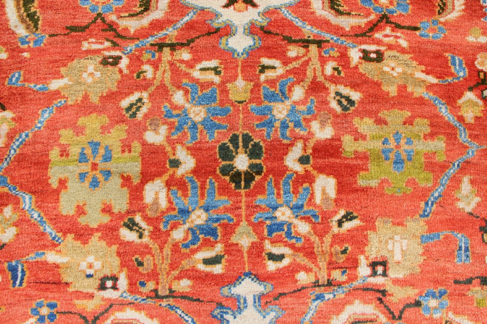 A large hand-knotted antique Ziegler carpet featuring a terracotta red field with floral palmettes framed by a wide indigo blue border. View V