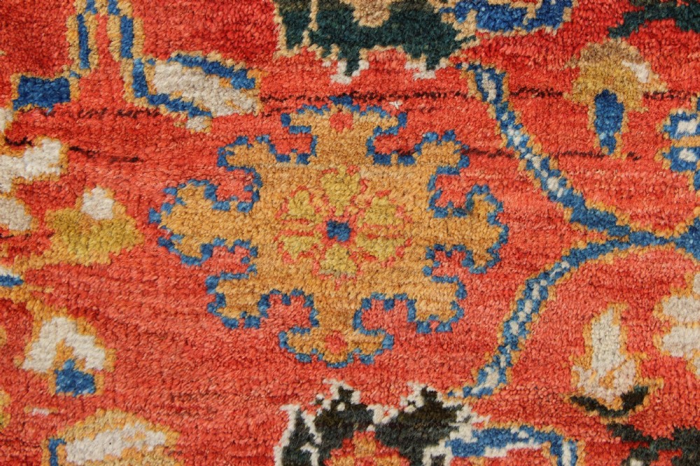 A large hand-knotted antique Ziegler carpet featuring a terracotta red field with floral palmettes framed by a wide indigo blue border. View VI
