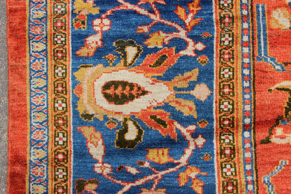 A large hand-knotted antique Ziegler carpet featuring a terracotta red field with floral palmettes framed by a wide indigo blue border. View VII