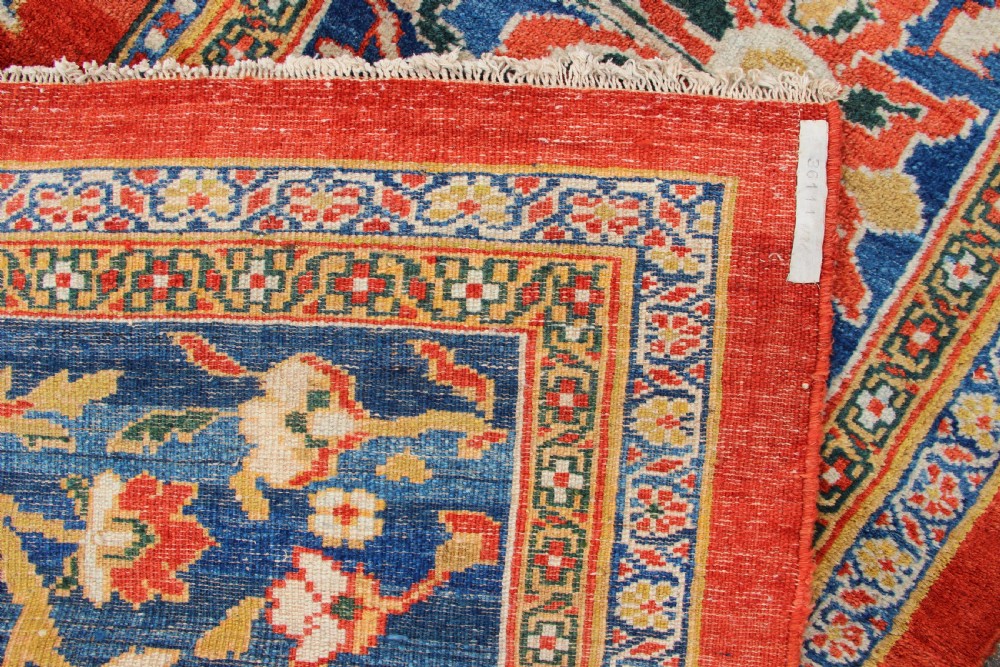 A large hand-knotted antique Ziegler carpet featuring a terracotta red field with floral palmettes framed by a wide indigo blue border. View IX