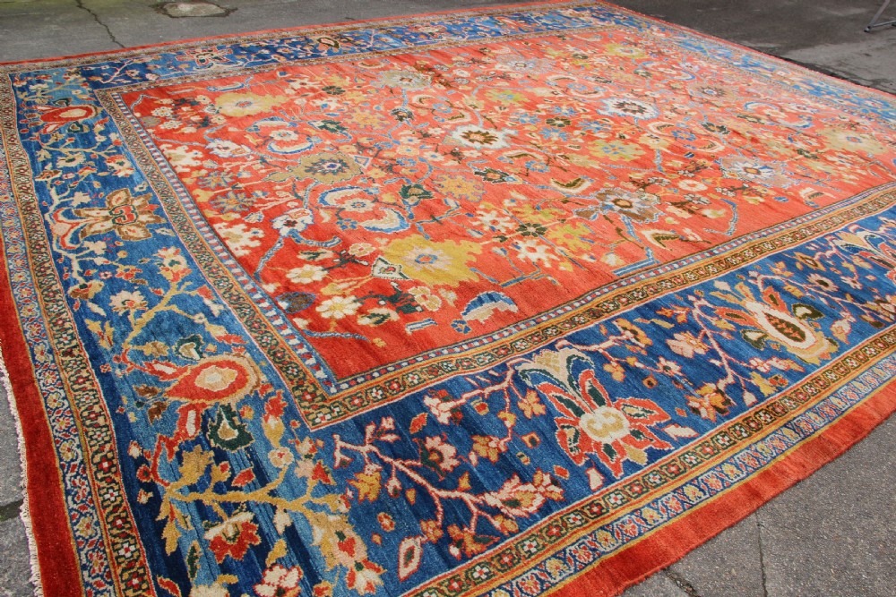 A large hand-knotted antique Ziegler carpet featuring a terracotta red field with floral palmettes framed by a wide indigo blue border. View X