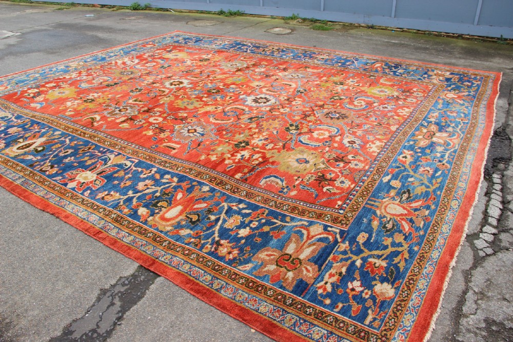 A large hand-knotted antique Ziegler carpet featuring a terracotta red field with floral palmettes framed by a wide indigo blue border. View XI