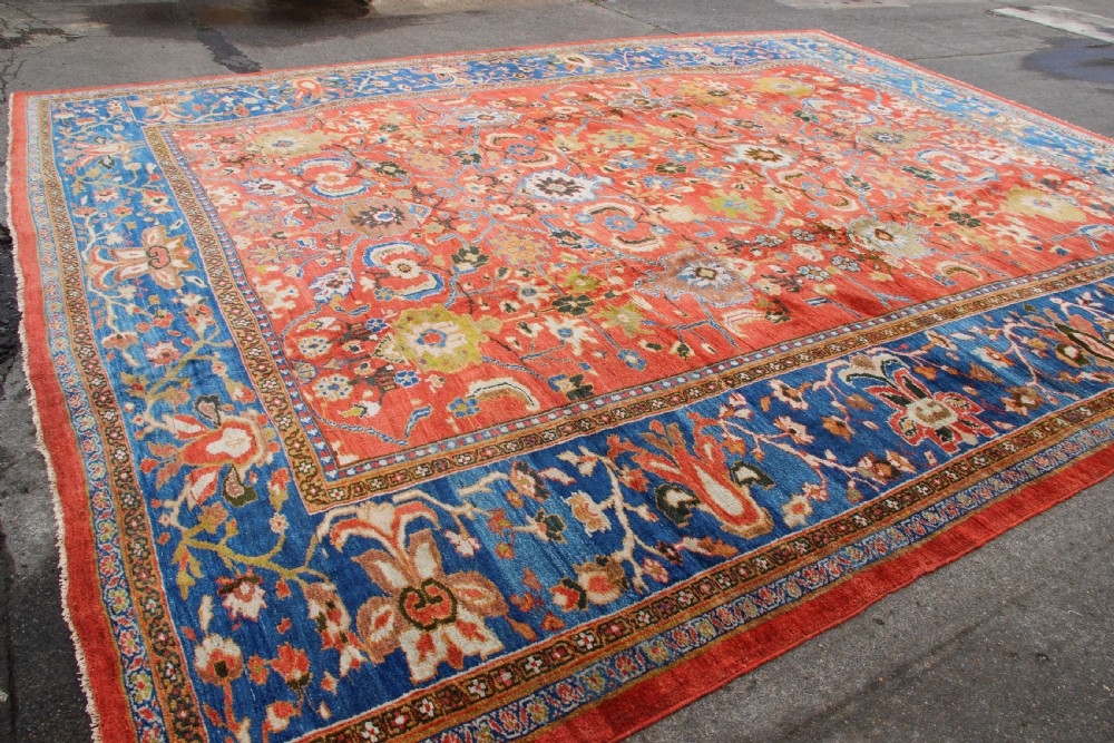 A large hand-knotted antique Ziegler carpet featuring a terracotta red field with floral palmettes framed by a wide indigo blue border. View XII