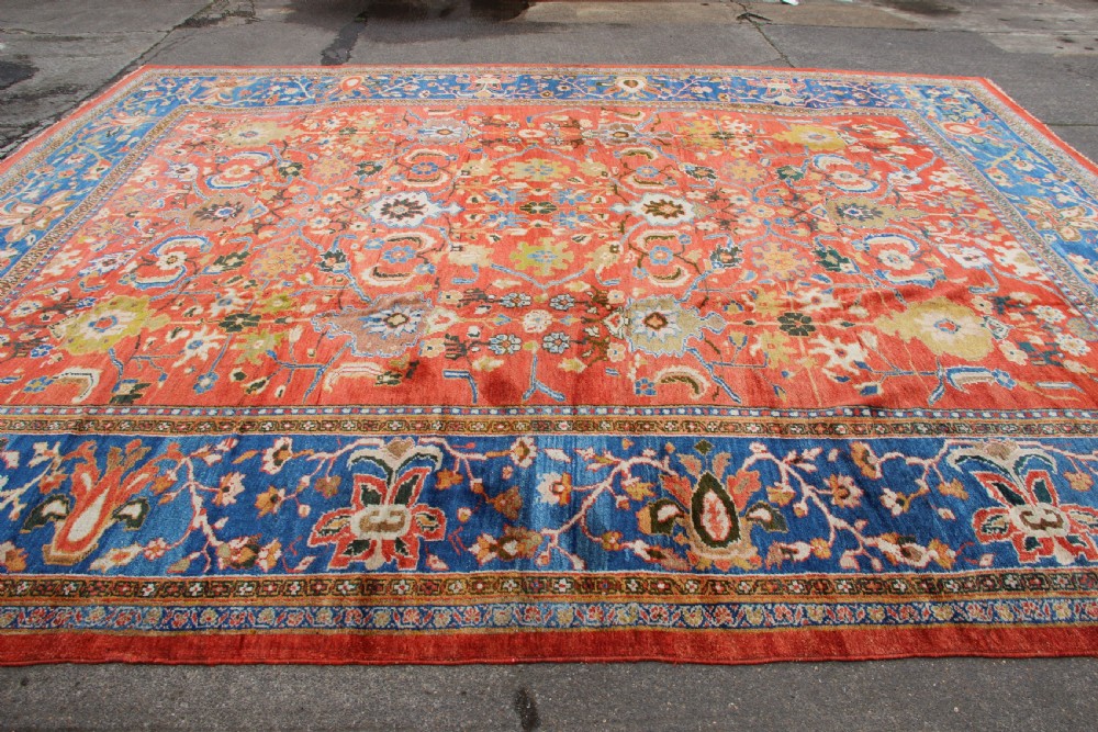 A large hand-knotted antique Ziegler carpet featuring a terracotta red field with floral palmettes framed by a wide indigo blue border. View XIII