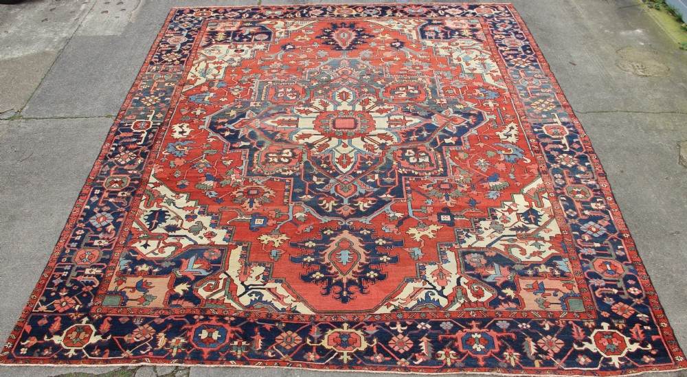 An oversized hand-knotted antique Karadja carpet featuring a large central geometric medallion on a rust red field surrounded by navy blue and cream borders.