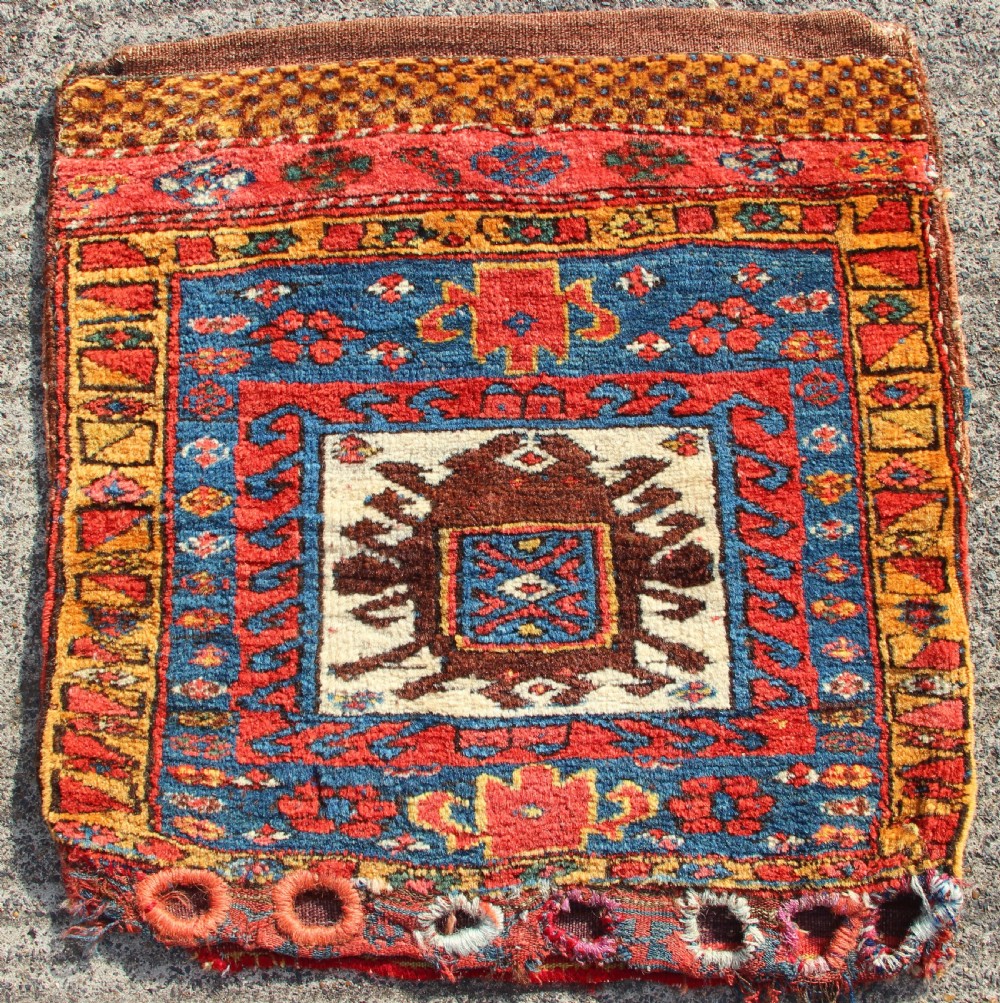 A square antique Kurdish woven saddlebag face displaying geometric borders in blue, red, and yellow surrounding a central medallion with woven bottom loops.