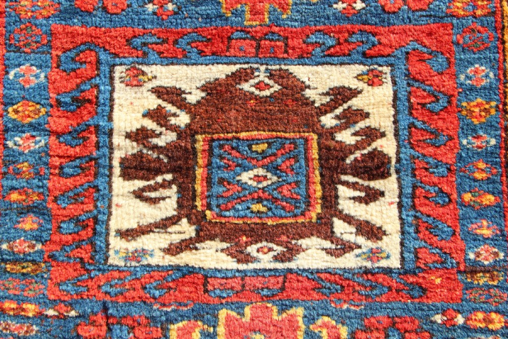 A square antique Kurdish woven saddlebag face displaying geometric borders in blue, red, and yellow surrounding a central medallion with woven bottom loops. View II