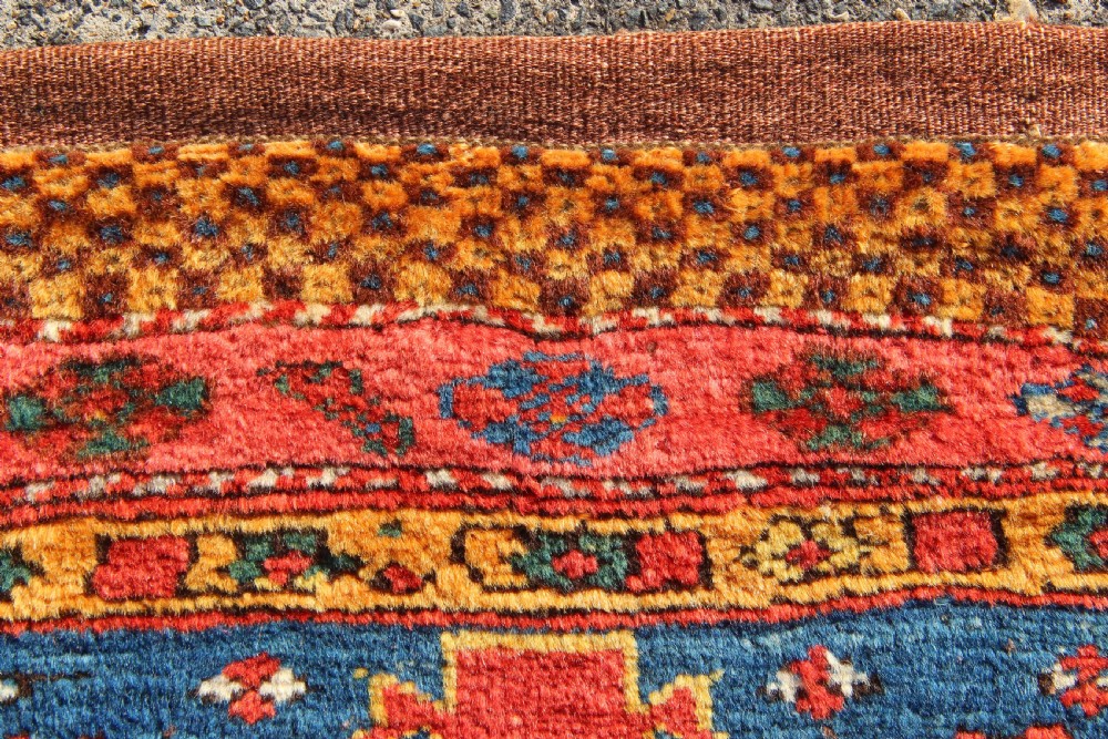 A square antique Kurdish woven saddlebag face displaying geometric borders in blue, red, and yellow surrounding a central medallion with woven bottom loops. View III