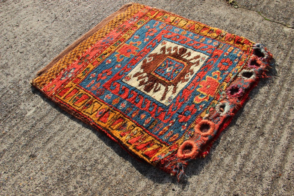 A square antique Kurdish woven saddlebag face displaying geometric borders in blue, red, and yellow surrounding a central medallion with woven bottom loops. View IV