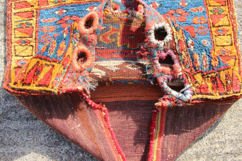 A square antique Kurdish woven saddlebag face displaying geometric borders in blue, red, and yellow surrounding a central medallion with woven bottom loops. View V