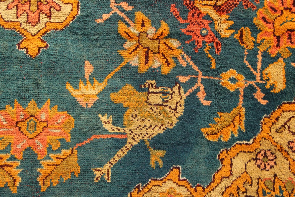 A large hand-knotted antique Oushak wool carpet featuring a central stepped medallion on a teal field surrounded by cream and gold floral borders. View IV