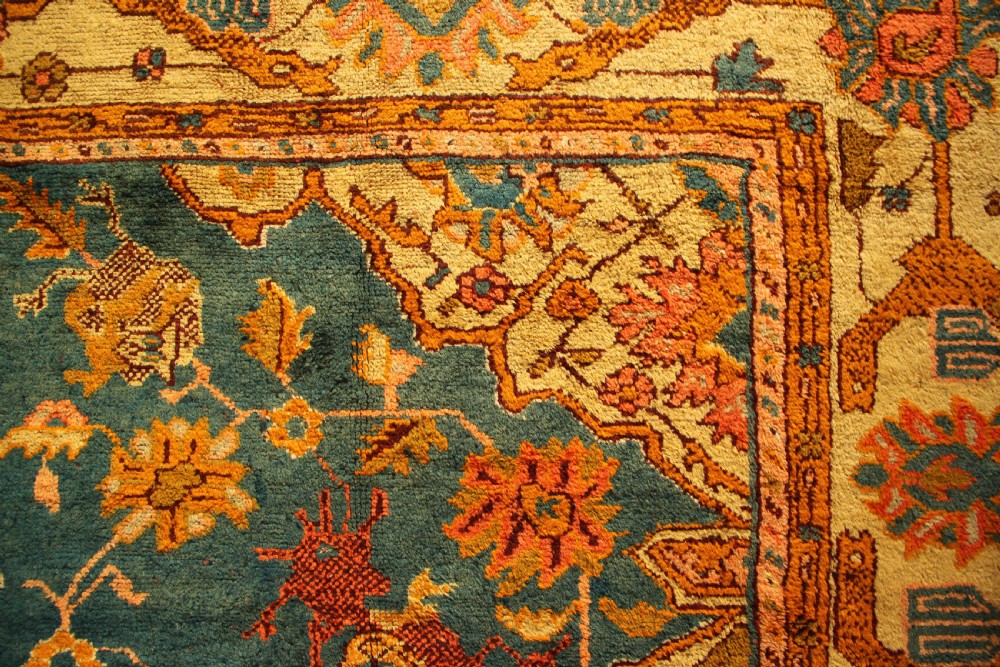 A large hand-knotted antique Oushak wool carpet featuring a central stepped medallion on a teal field surrounded by cream and gold floral borders. View V