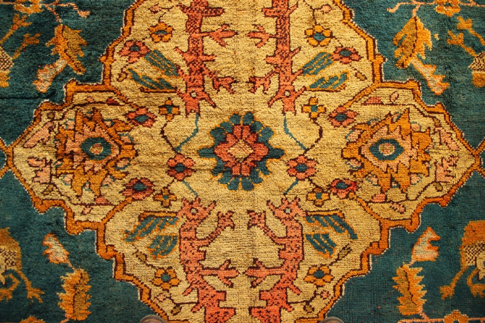 A large hand-knotted antique Oushak wool carpet featuring a central stepped medallion on a teal field surrounded by cream and gold floral borders. View VI
