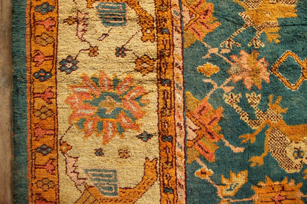 A large hand-knotted antique Oushak wool carpet featuring a central stepped medallion on a teal field surrounded by cream and gold floral borders. View VII