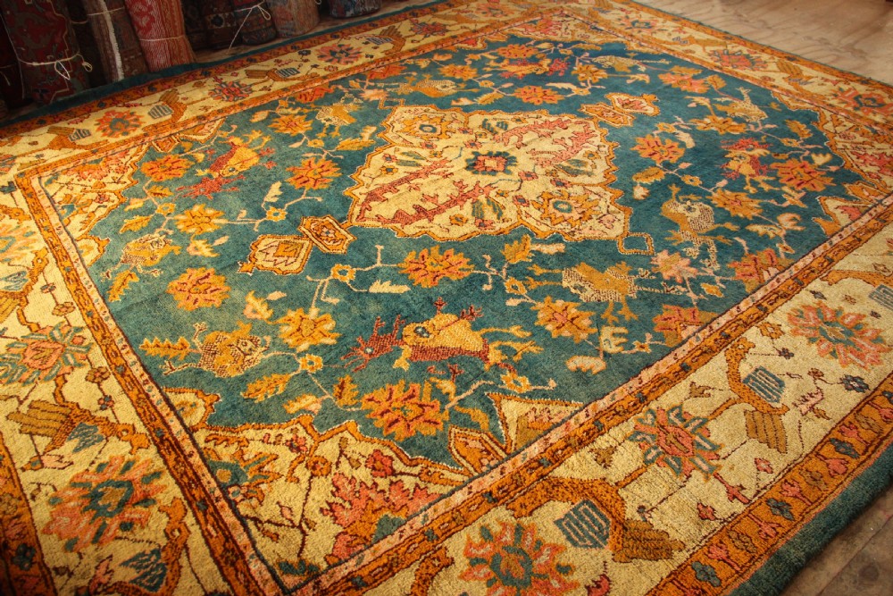 A large hand-knotted antique Oushak wool carpet featuring a central stepped medallion on a teal field surrounded by cream and gold floral borders. View VIII