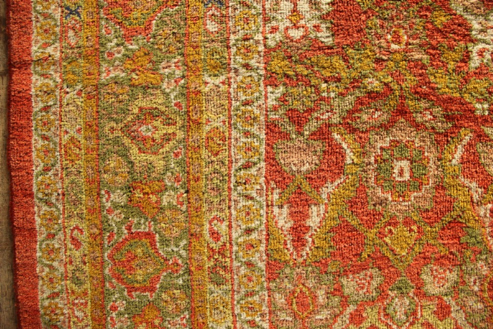 A square hand-knotted antique Ziegler wool carpet featuring a terracotta red field filled with intricate floral palmettes and framed by multi-tiered decorative borders. View X