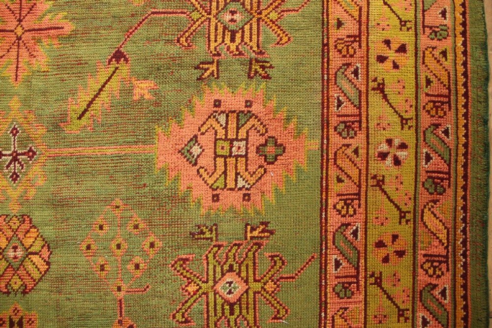 A large hand-knotted antique Oushak wool carpet featuring an olive green field with salmon pink geometric motifs and a yellow patterned border. View III