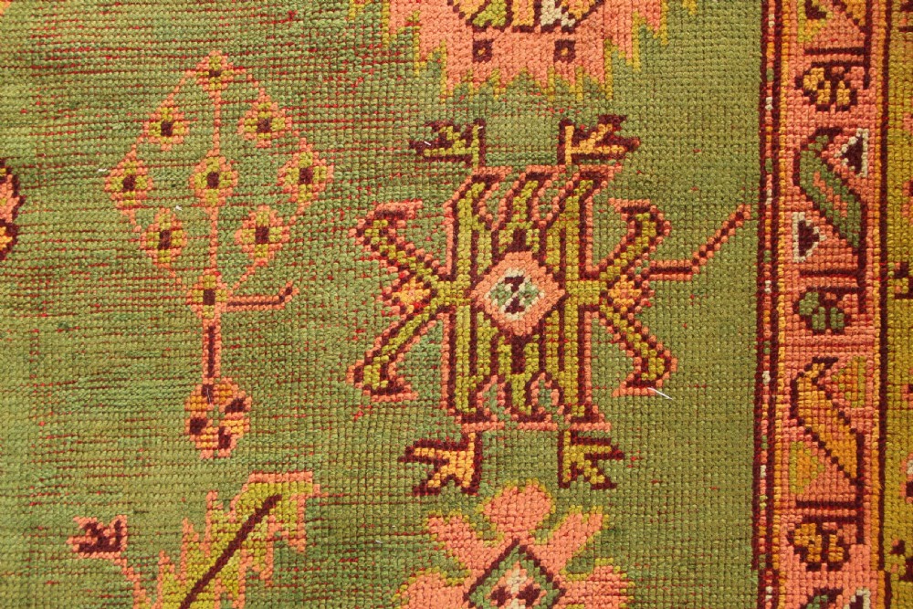 A large hand-knotted antique Oushak wool carpet featuring an olive green field with salmon pink geometric motifs and a yellow patterned border. View V