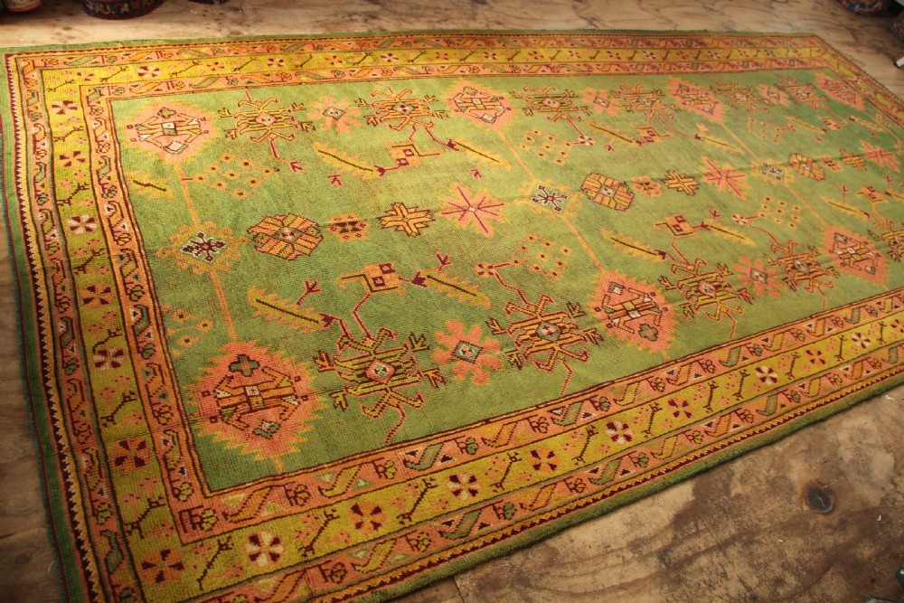 A large hand-knotted antique Oushak wool carpet featuring an olive green field with salmon pink geometric motifs and a yellow patterned border. View VI