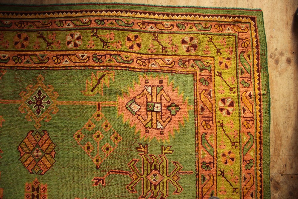 A large hand-knotted antique Oushak wool carpet featuring an olive green field with salmon pink geometric motifs and a yellow patterned border. View VII