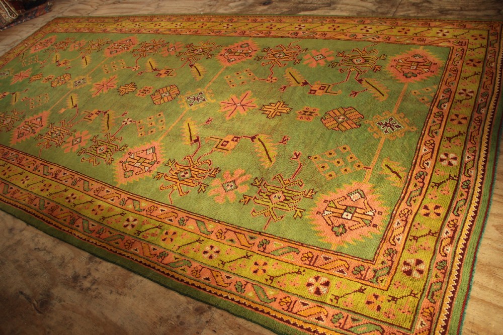 A large hand-knotted antique Oushak wool carpet featuring an olive green field with salmon pink geometric motifs and a yellow patterned border. View VIII
