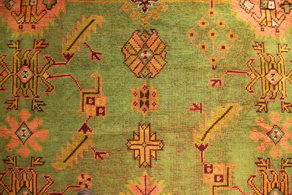 A large hand-knotted antique Oushak wool carpet featuring an olive green field with salmon pink geometric motifs and a yellow patterned border. View IX