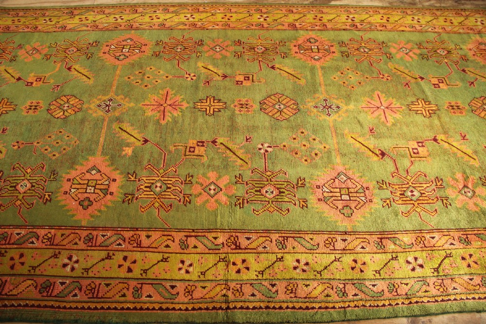 A large hand-knotted antique Oushak wool carpet featuring an olive green field with salmon pink geometric motifs and a yellow patterned border. View X