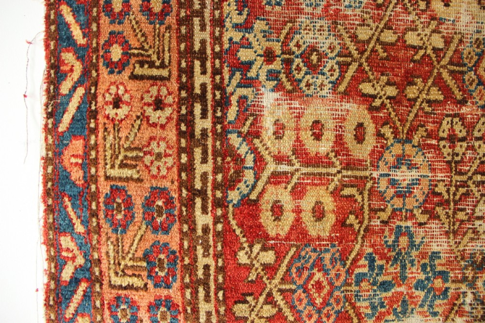 An antique hand-knotted textile fragment displaying geometric patterns and floral motifs in shades of terracotta red, indigo blue, and cream. View II
