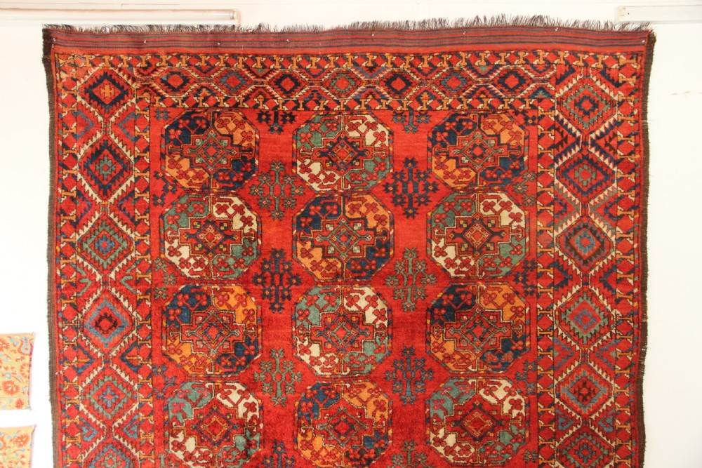 A large hand-knotted wool carpet featuring repeating octagonal gul medallions and geometric borders in terracotta red, navy blue, and cream tones. View II