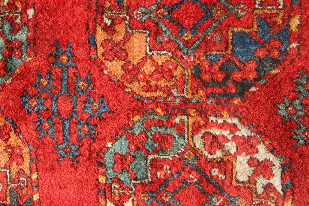 A large hand-knotted wool carpet featuring repeating octagonal gul medallions and geometric borders in terracotta red, navy blue, and cream tones. View VII
