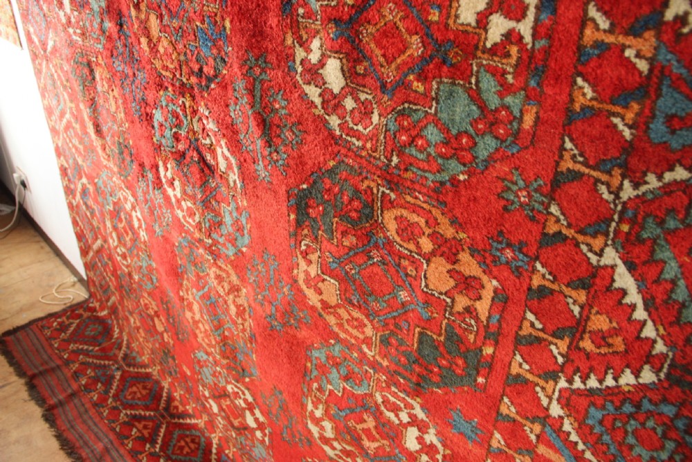 A large hand-knotted wool carpet featuring repeating octagonal gul medallions and geometric borders in terracotta red, navy blue, and cream tones. View IX