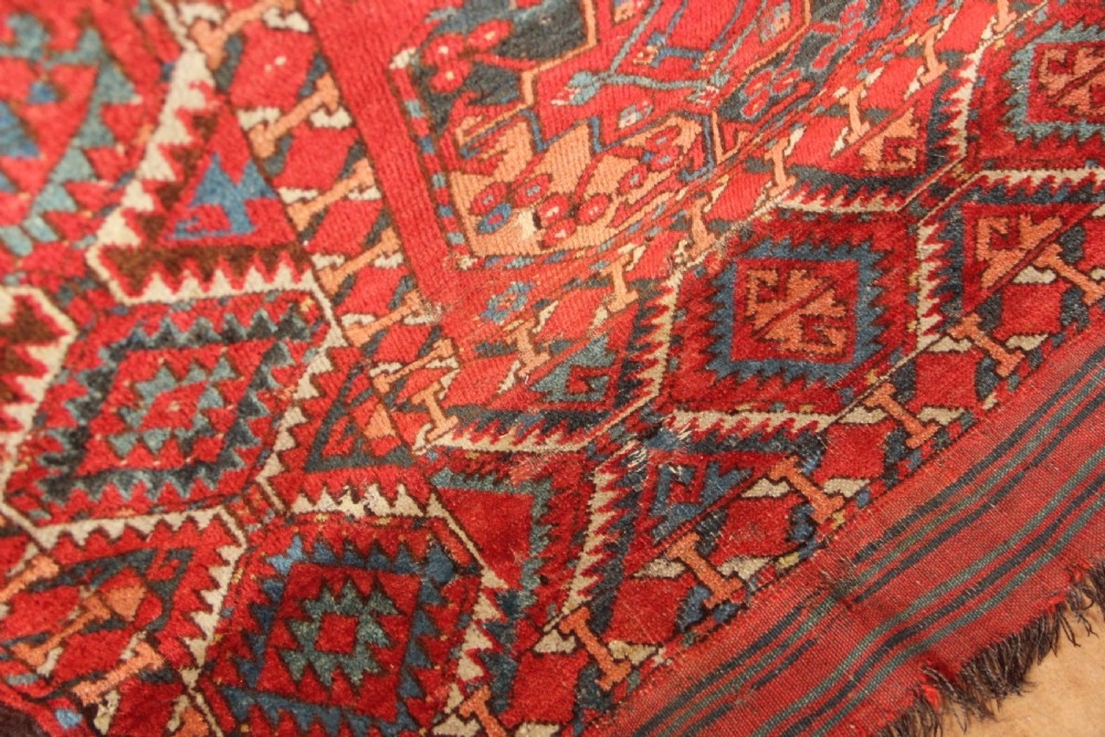 A large hand-knotted wool carpet featuring repeating octagonal gul medallions and geometric borders in terracotta red, navy blue, and cream tones. View X