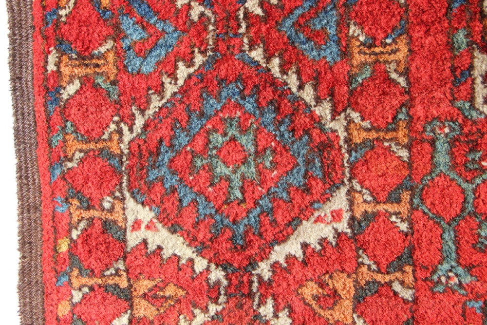 A large hand-knotted wool carpet featuring repeating octagonal gul medallions and geometric borders in terracotta red, navy blue, and cream tones. View XII