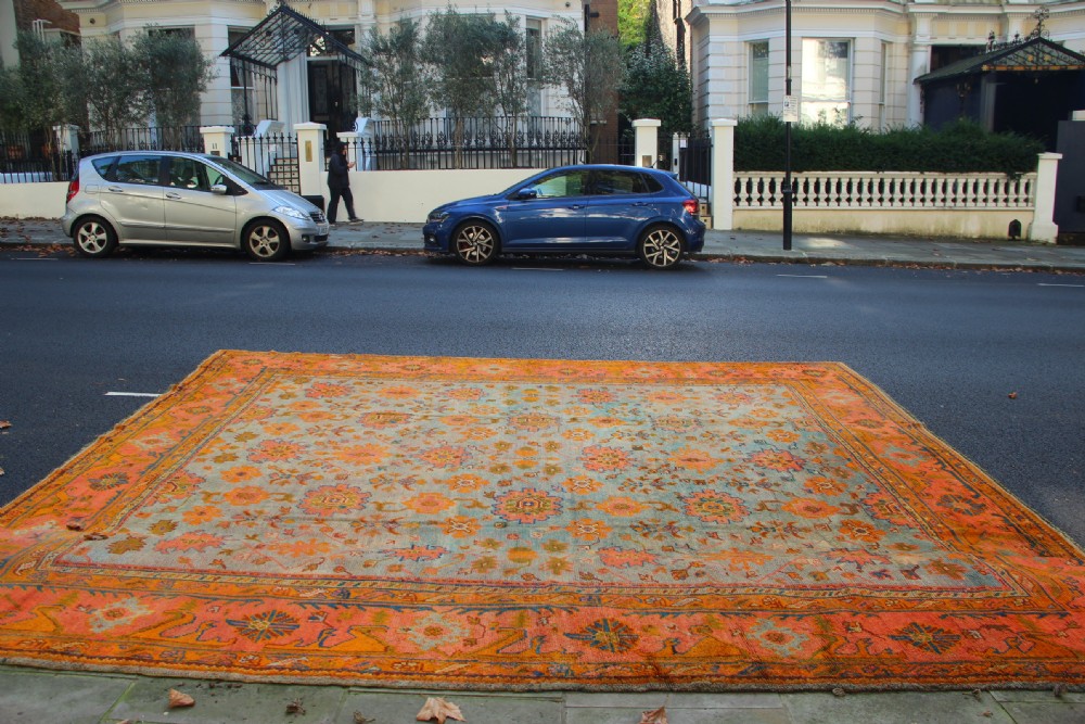 A large square antique Oushak rug with a light blue central field decorated with floral medallions and a wide terracotta and orange floral border. View V