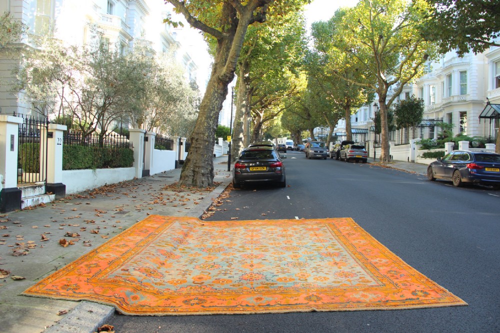 A large square antique Oushak rug with a light blue central field decorated with floral medallions and a wide terracotta and orange floral border. View IX