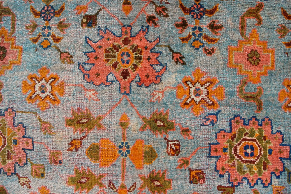 A large square antique Oushak rug with a light blue central field decorated with floral medallions and a wide terracotta and orange floral border. View XI