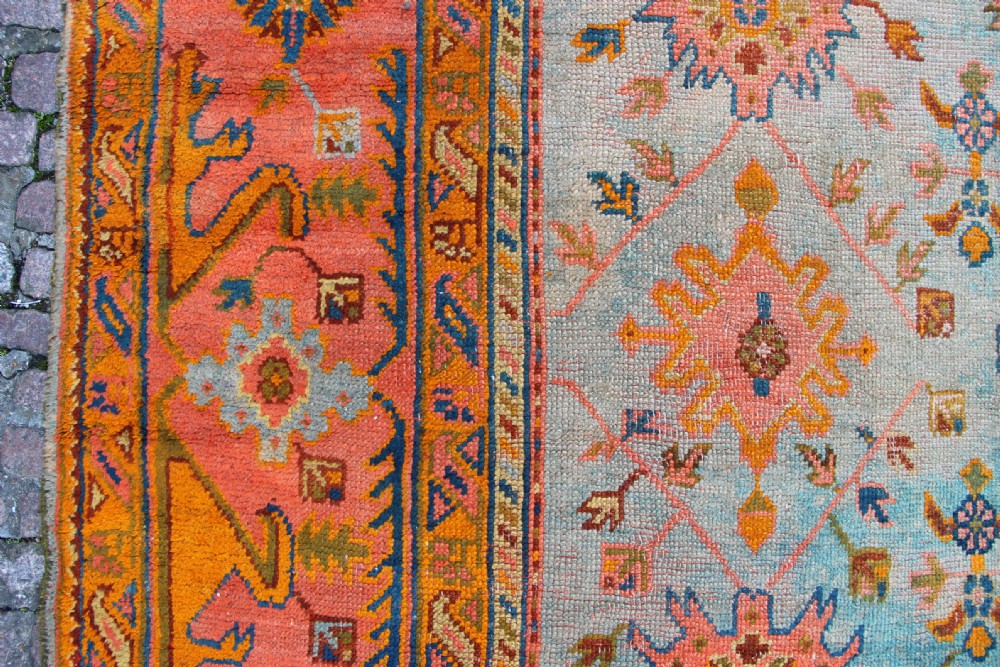 A large square antique Oushak rug with a light blue central field decorated with floral medallions and a wide terracotta and orange floral border. View XII