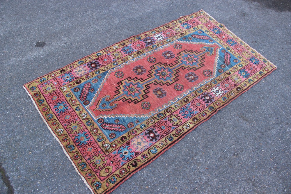 A rectangular hand-knotted antique Bakshaish Persian rug featuring a central terracotta stepped medallion field with blue spandrels and patterned floral borders. View VII
