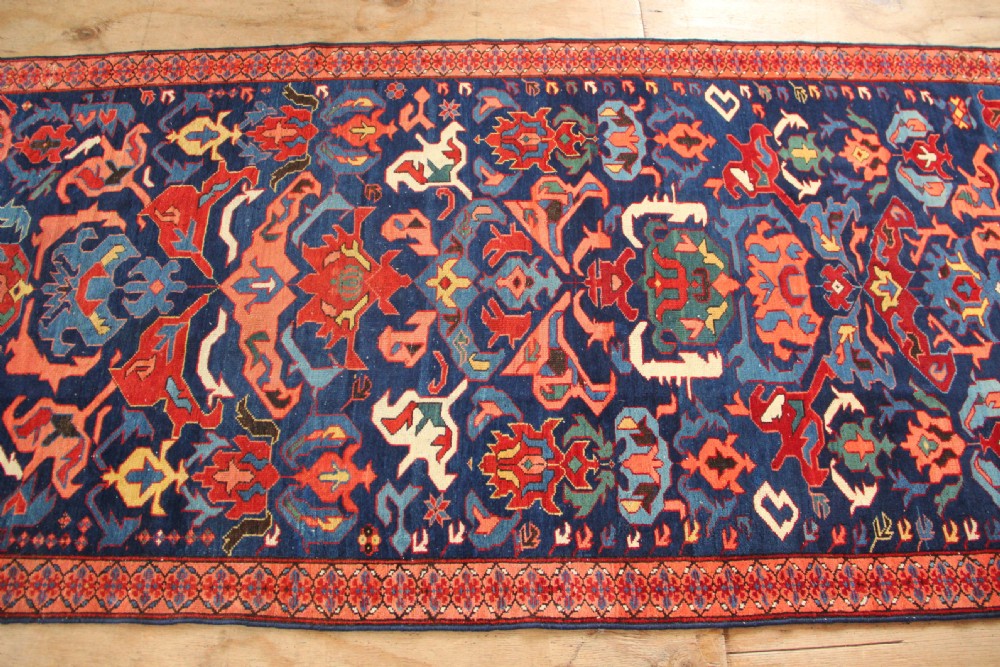 A long hand-knotted antique Caucasian Seychour rug featuring a navy blue field with red and coral geometric cross motifs and a patterned red border. View VI