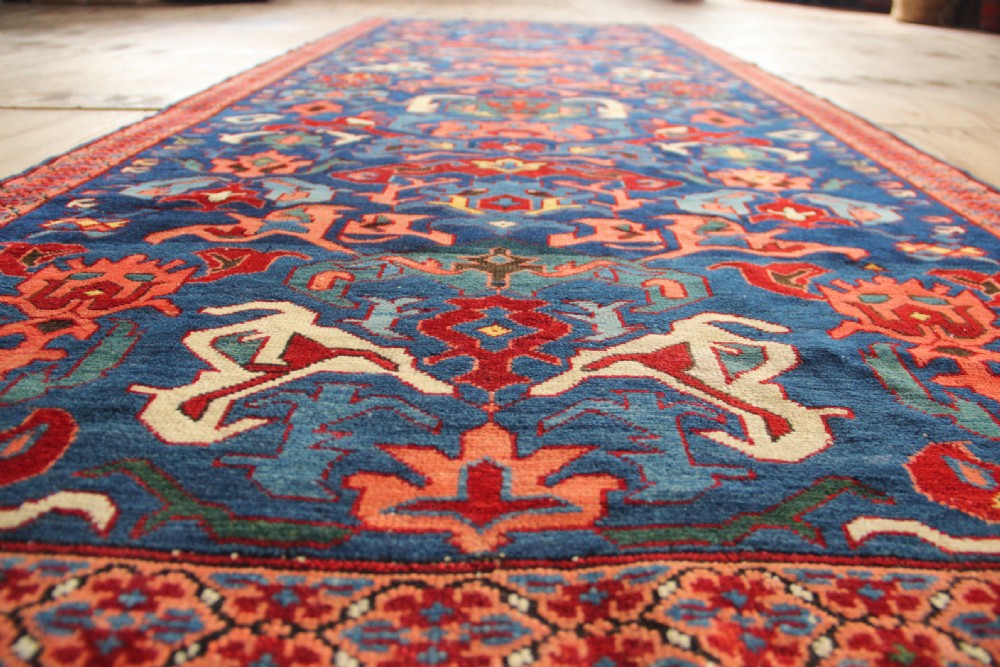 A long hand-knotted antique Caucasian Seychour rug featuring a navy blue field with red and coral geometric cross motifs and a patterned red border. View X
