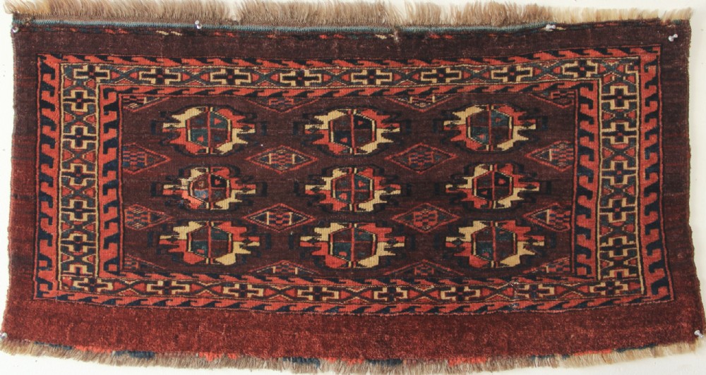 An antique hand-woven Yomud Mafrash wool textile panel featuring repeating geometric gul motifs in dark red, cream, and blue tones.
