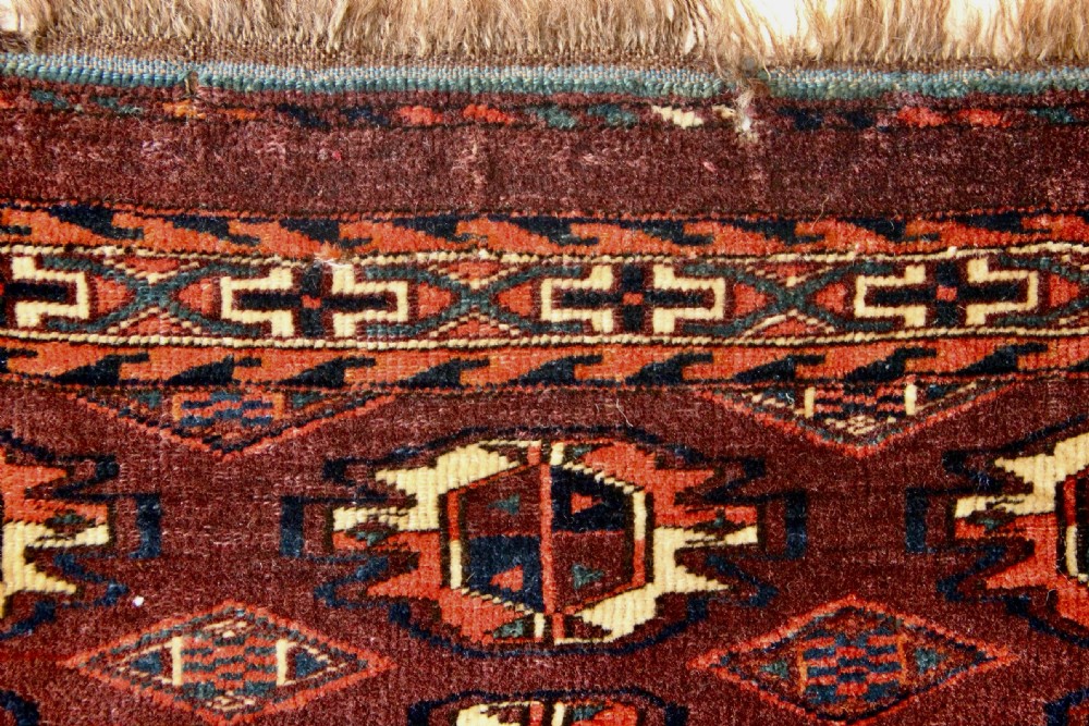 An antique hand-woven Yomud Mafrash wool textile panel featuring repeating geometric gul motifs in dark red, cream, and blue tones. View V