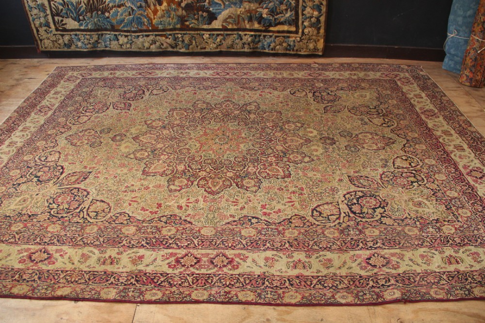 A large hand-knotted Persian Lavar Kirman carpet featuring a complex central floral medallion, intricate corner spandrels, and multi-layered decorative borders in cream, rose pink, and navy blue. View IV