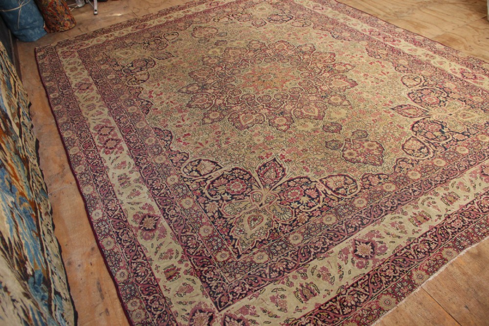 A large hand-knotted Persian Lavar Kirman carpet featuring a complex central floral medallion, intricate corner spandrels, and multi-layered decorative borders in cream, rose pink, and navy blue. View V