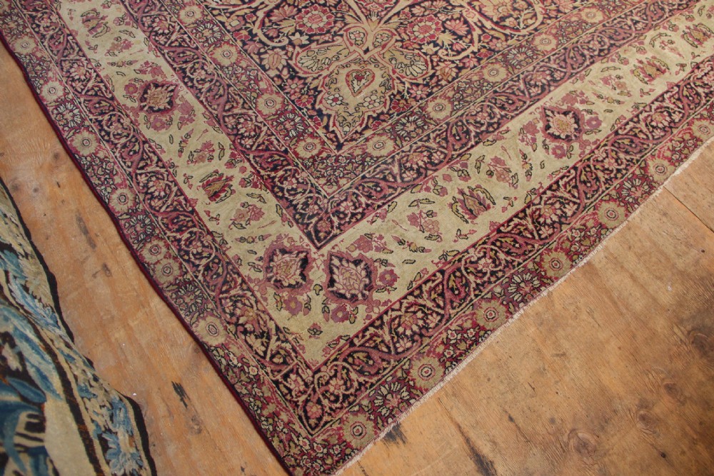 A large hand-knotted Persian Lavar Kirman carpet featuring a complex central floral medallion, intricate corner spandrels, and multi-layered decorative borders in cream, rose pink, and navy blue. View VI