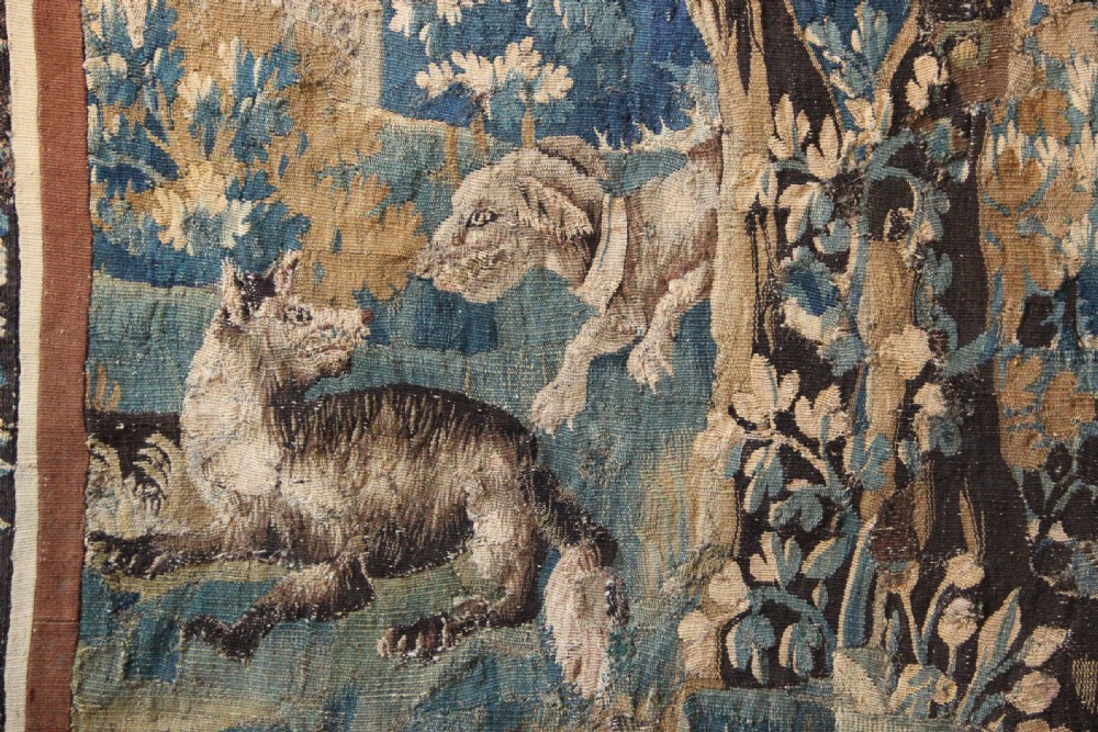 A large 18th-century hand-woven verdure tapestry depicting a dense woodland scene with foliage, animals, and distant architecture within a decorative floral border. View III