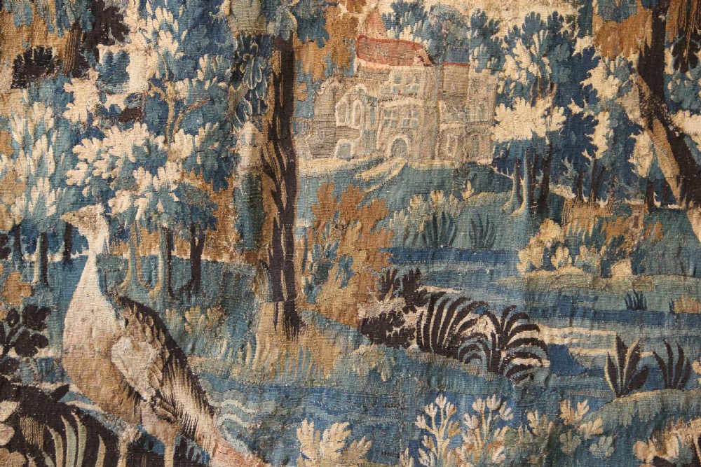 A large 18th-century hand-woven verdure tapestry depicting a dense woodland scene with foliage, animals, and distant architecture within a decorative floral border. View IV
