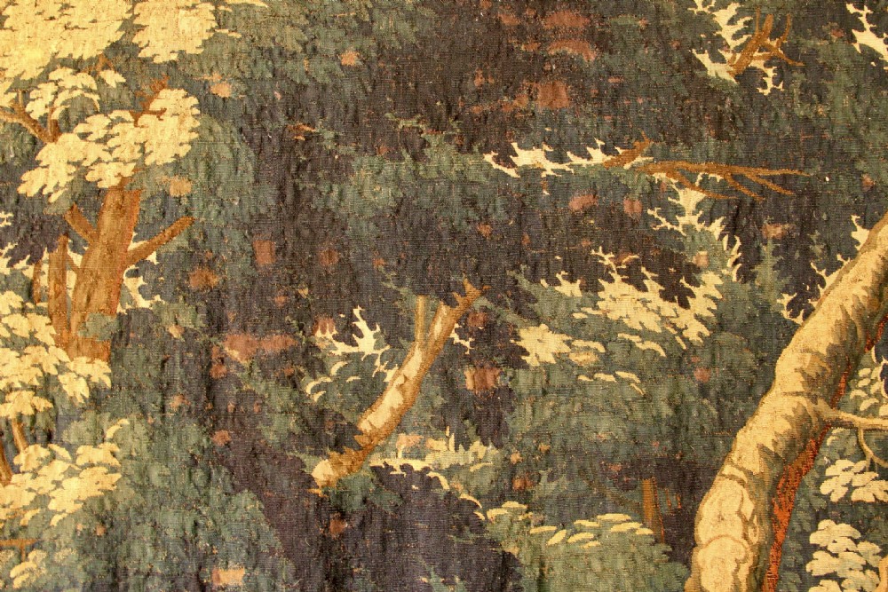 An 18th century verdure tapestry depicting a dense woodland scene with mature trees, foliage, and a distant landscape in muted greens and browns. View VI